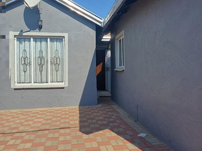 A paved rear courtyard area featuring grey exterior walls, security bars on the window, and a satellite dish installation.