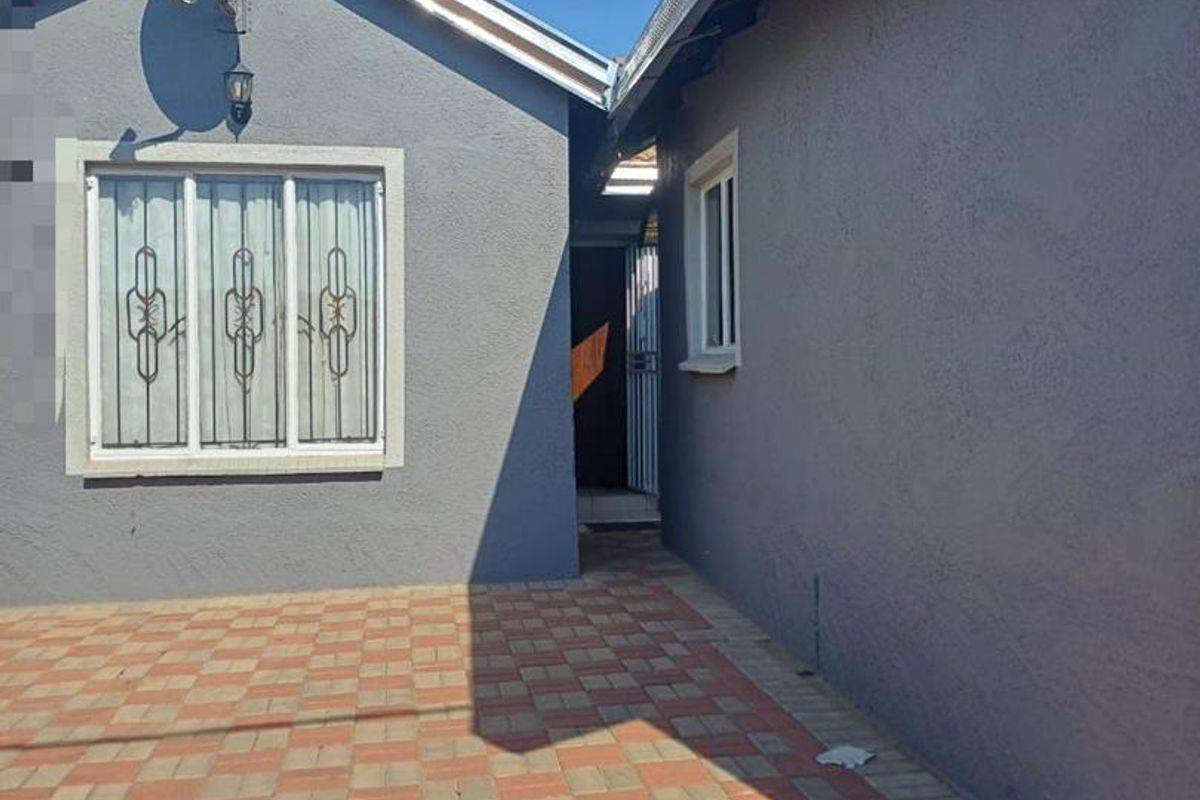 A paved rear courtyard area featuring grey exterior walls, security bars on the window, and a satellite dish installation.