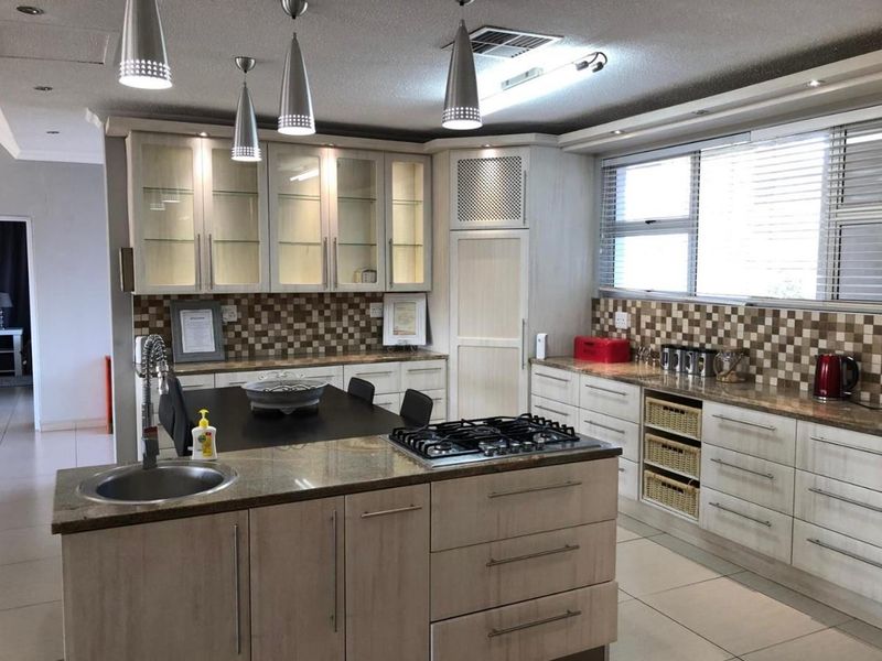 A well-appointed kitchen featuring granite countertops, a central island with a gas hob, ample built-in cabinetry, and modern pendant lighting.