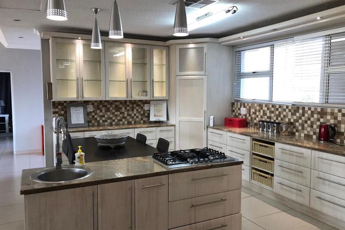 A well-appointed kitchen featuring granite countertops, a central island with a gas hob, ample built-in cabinetry, and modern pendant lighting.