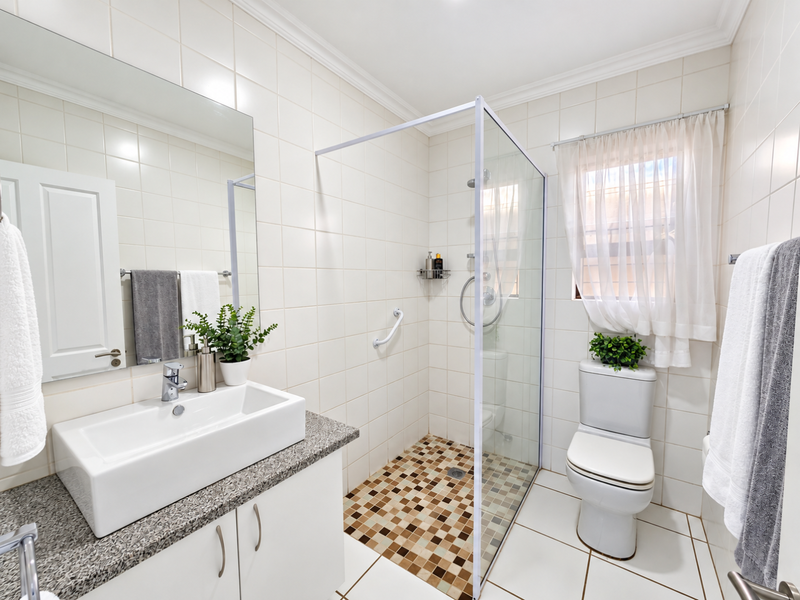 A well-maintained bathroom featuring a modern vanity with granite countertop, a walk-in shower with mosaic tiling, and a standard toilet.