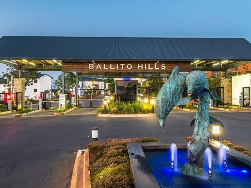 The main entrance gatehouse of Ballito Hills, featuring a prominent dolphin sculpture water feature and modern architectural lighting at dusk.