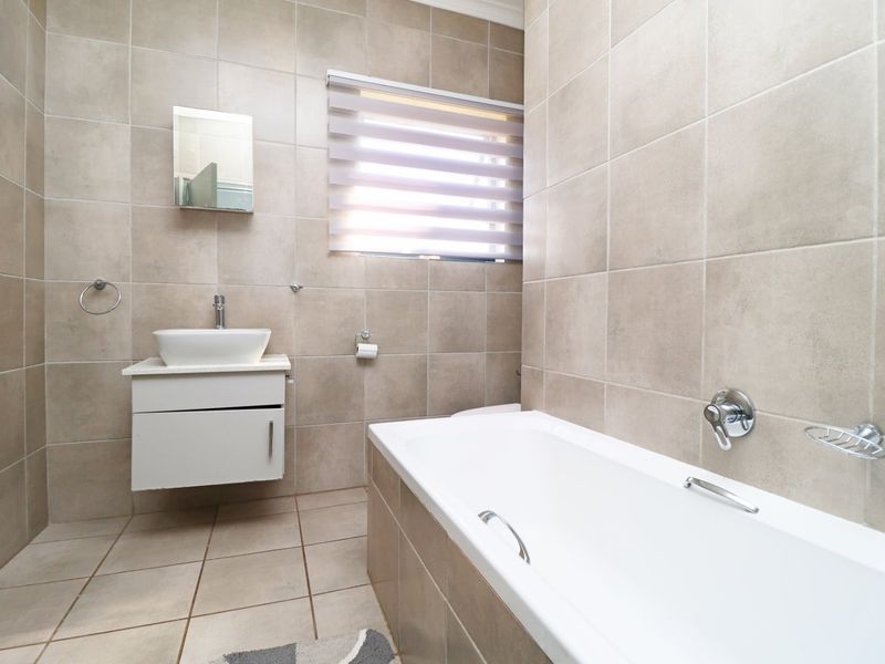 A modern, well-maintained bathroom featuring neutral floor-to-ceiling tiling, a wall-mounted vanity with a vessel sink, and a clean white bathtub.
