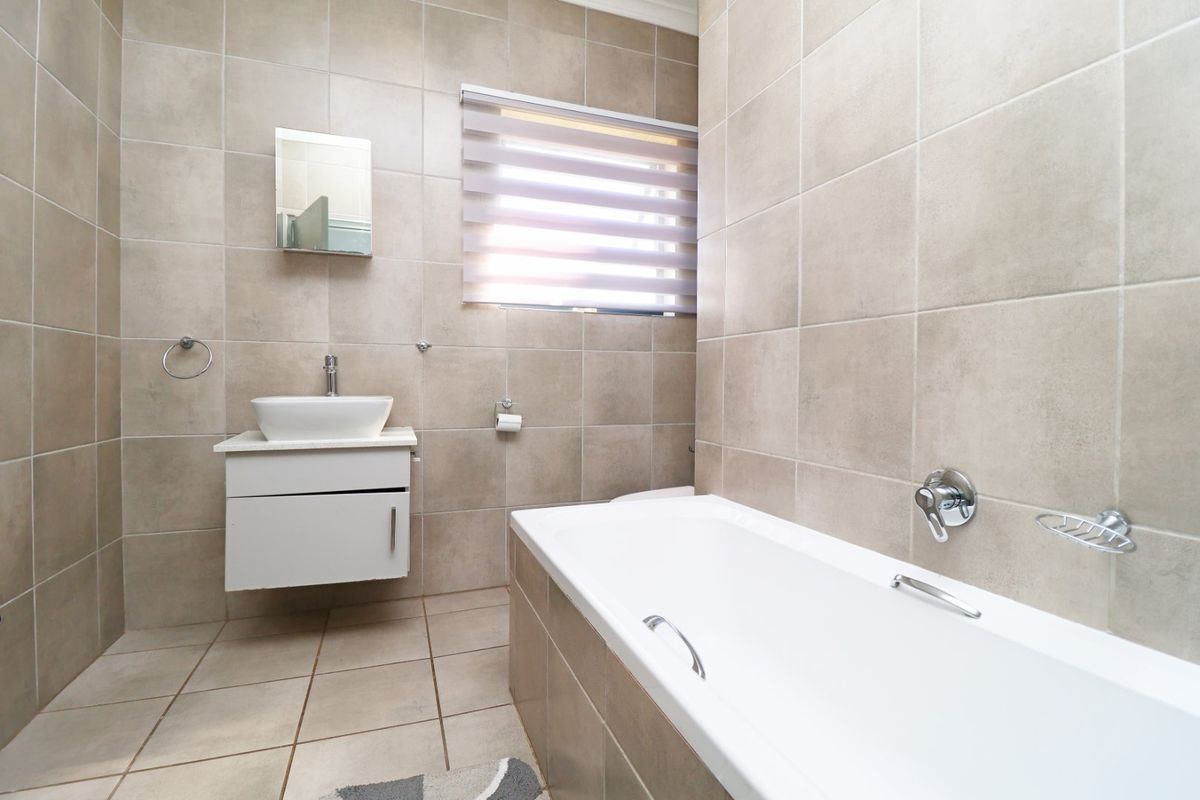 A modern, well-maintained bathroom featuring neutral floor-to-ceiling tiling, a wall-mounted vanity with a vessel sink, and a clean white bathtub.