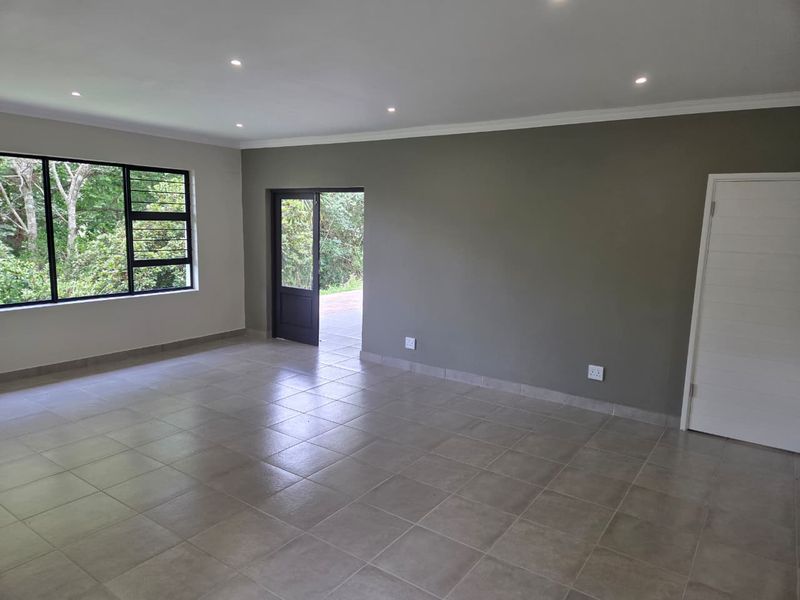 A spacious, empty living area featuring neutral tiled flooring, recessed downlighting, and direct access to the exterior through a glass-panelled door.