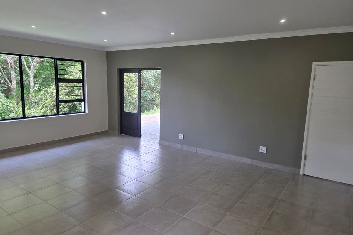 A spacious, empty living area featuring neutral tiled flooring, recessed downlighting, and direct access to the exterior through a glass-panelled door.