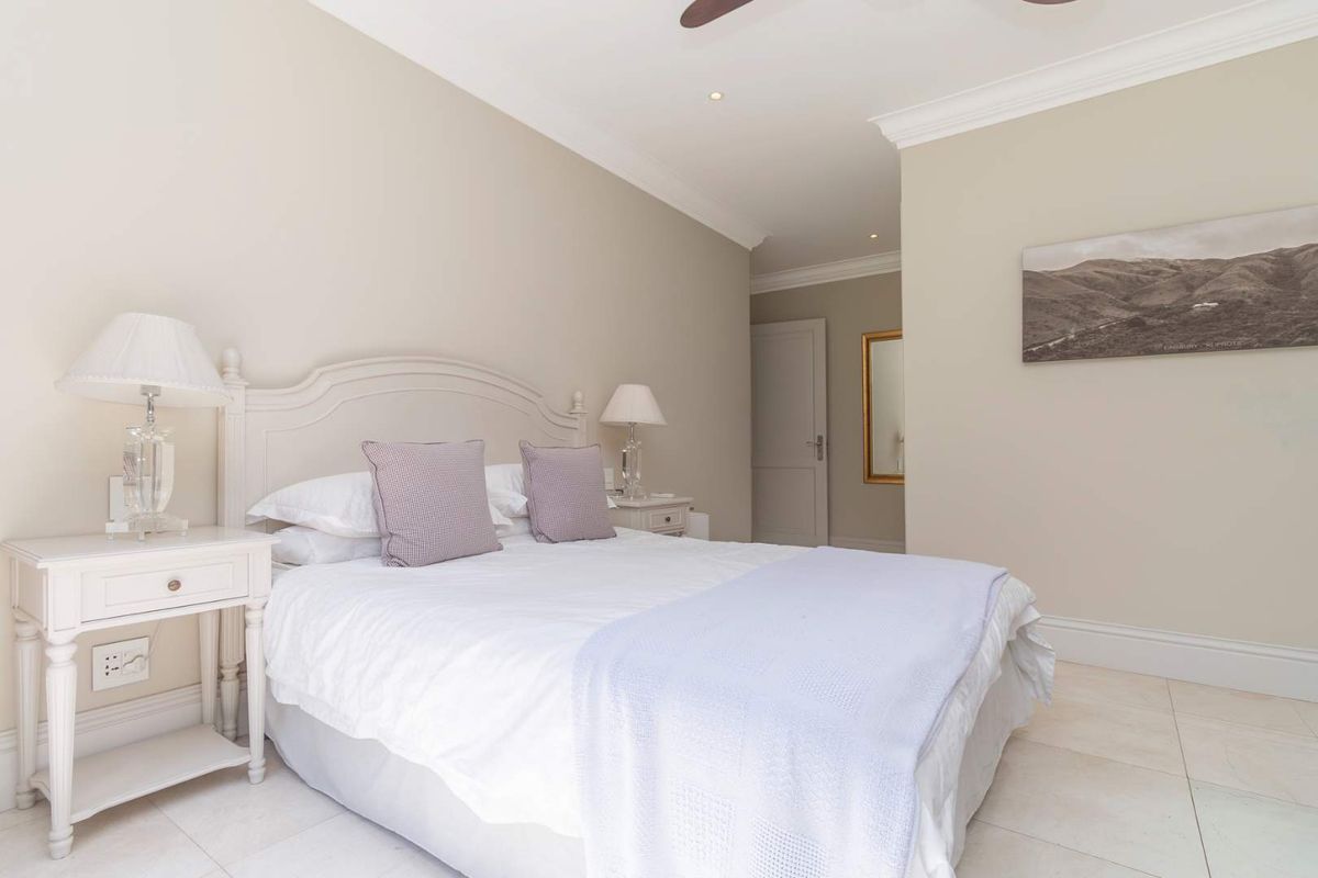 A well-maintained bedroom featuring neutral wall tones, crown molding, recessed lighting, and tiled flooring, creating a bright and comfortable living space.