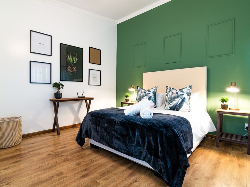 A well-presented bedroom featuring laminate flooring, a green accent wall with decorative molding, and classic ceiling coving.