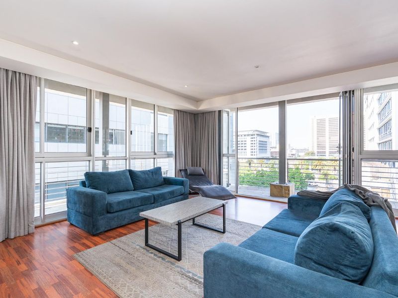 Spacious living room featuring hardwood flooring, recessed lighting, and expansive floor-to-ceiling windows that provide abundant natural light and access to the balcony.