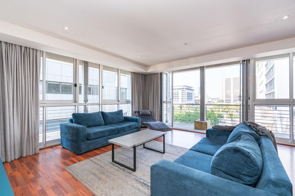 Spacious living room featuring hardwood flooring, recessed lighting, and expansive floor-to-ceiling windows that provide abundant natural light and access to the balcony.