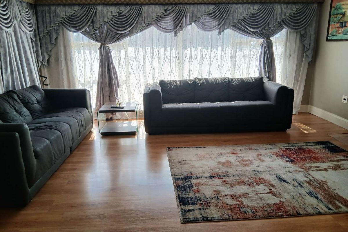 A living room featuring laminate flooring and a large window with decorative drapery.