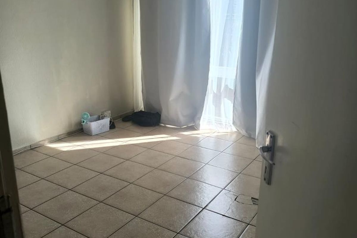 A vacant bedroom featuring tiled flooring and a sliding door leading to an outdoor area, requiring minor cosmetic updates.