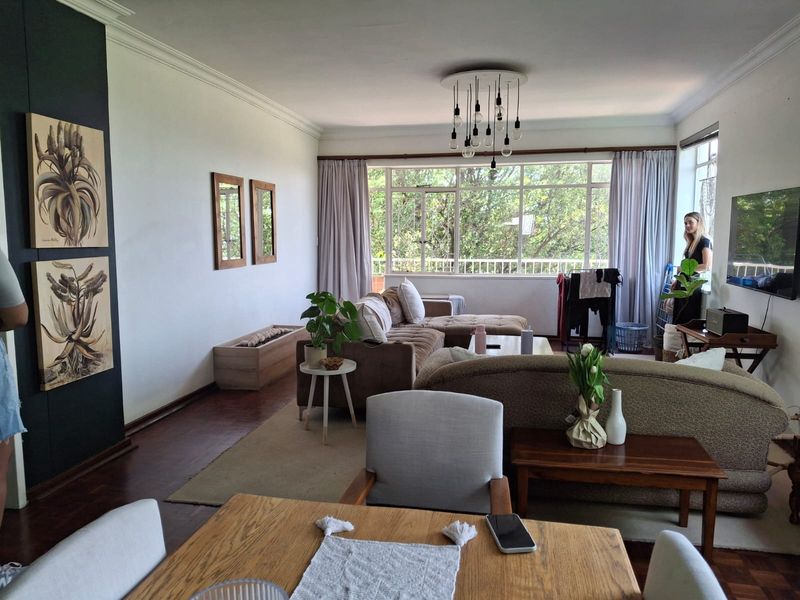 Spacious open-plan living area featuring classic parquet flooring, large windows providing natural light, and elegant ceiling cornicing.