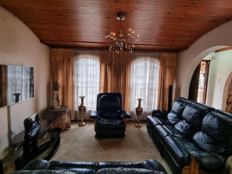 A cozy living room featuring a warm timber-clad ceiling, arched architectural details, and large windows with security bars.