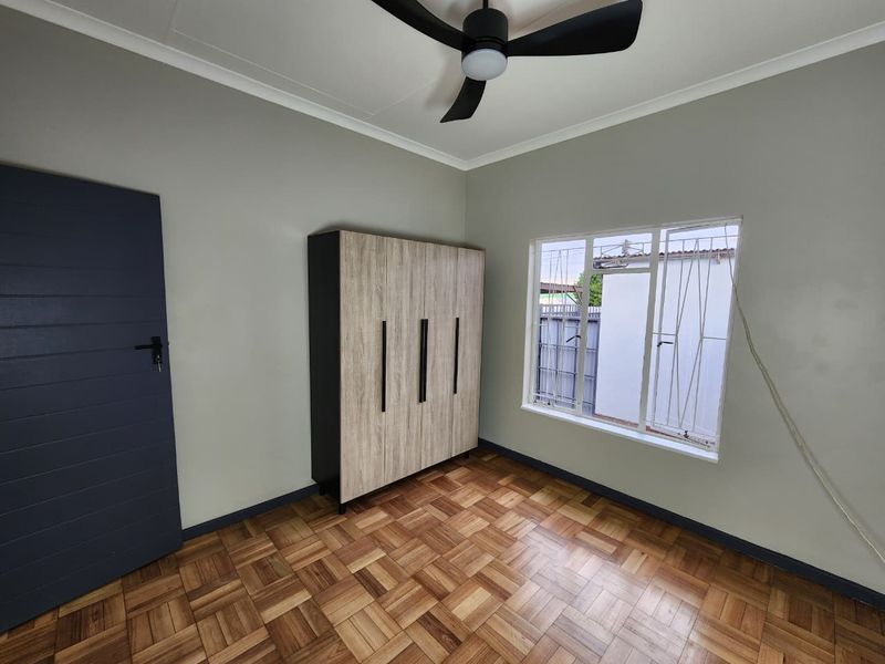 A bright, empty bedroom featuring polished parquet flooring, a modern ceiling fan, and a built-in wardrobe with contemporary finishes.