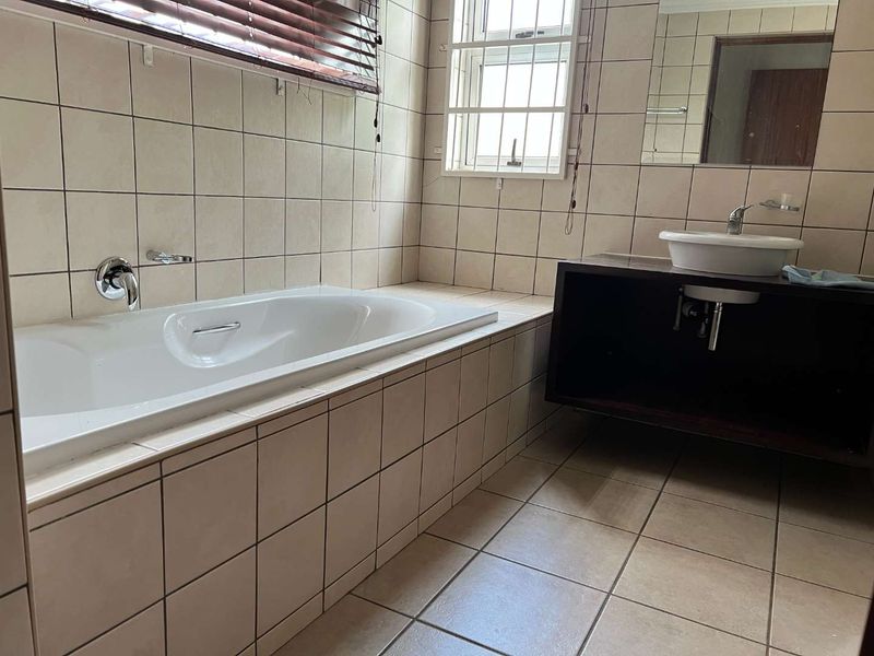 A functional bathroom featuring a built-in bathtub, wall-mounted basin with vanity cabinet, and neutral tiled finishes throughout.