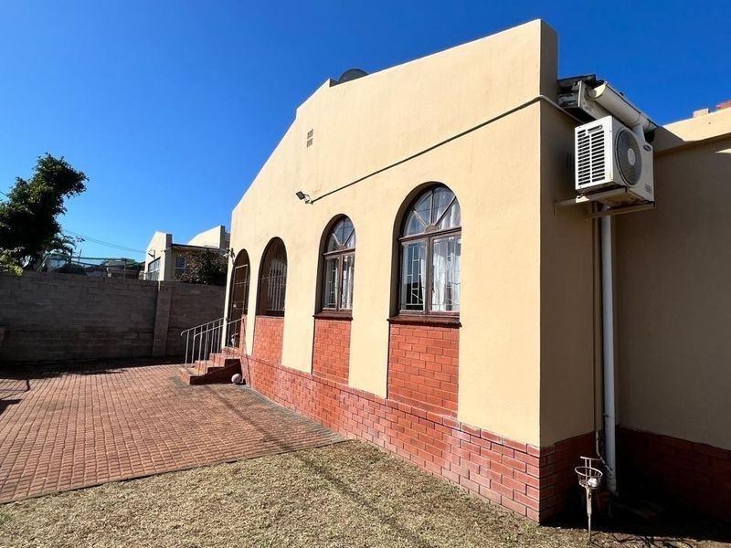 Rear exterior view of the property featuring brick paving, arched windows, and an installed air conditioning unit.