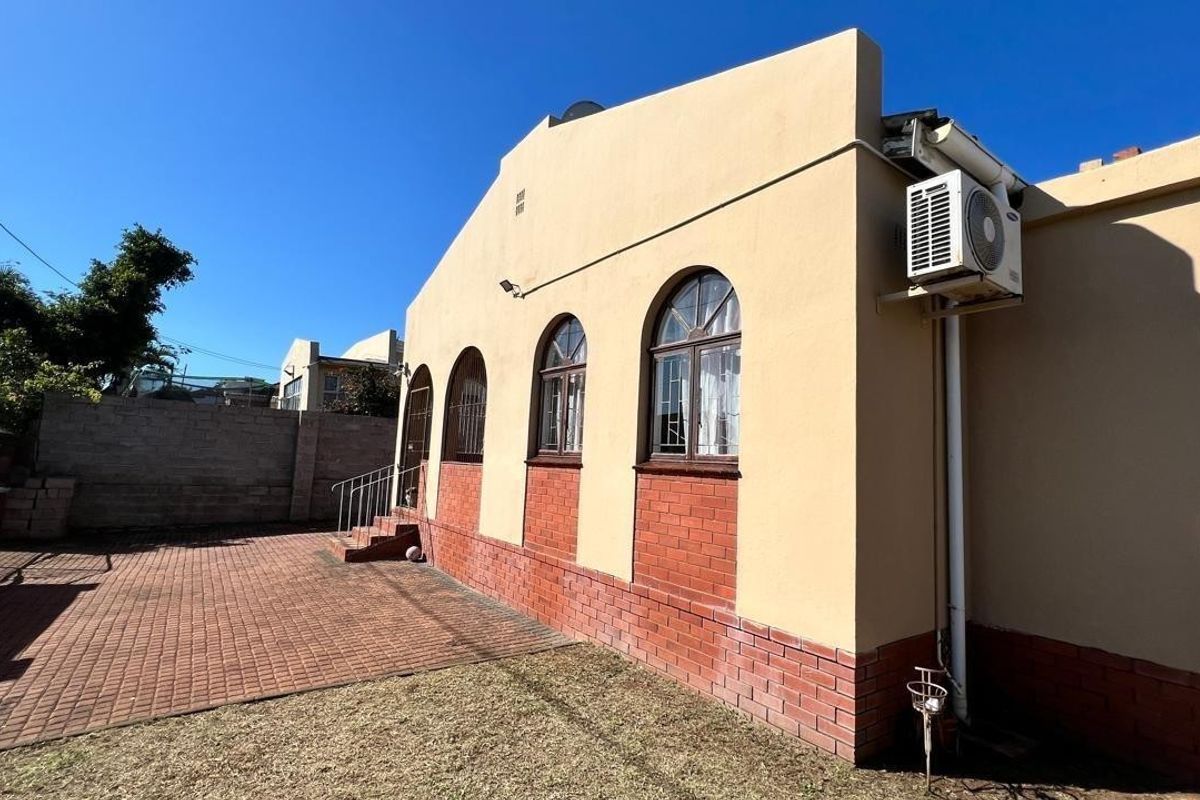 Rear exterior view of the property featuring brick paving, arched windows, and an installed air conditioning unit.