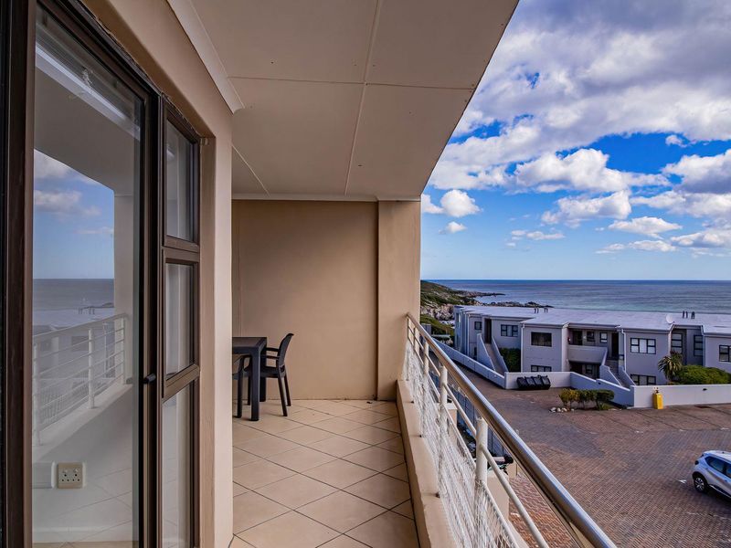 A spacious covered balcony featuring tiled flooring and a metal balustrade, offering expansive coastal and complex views.