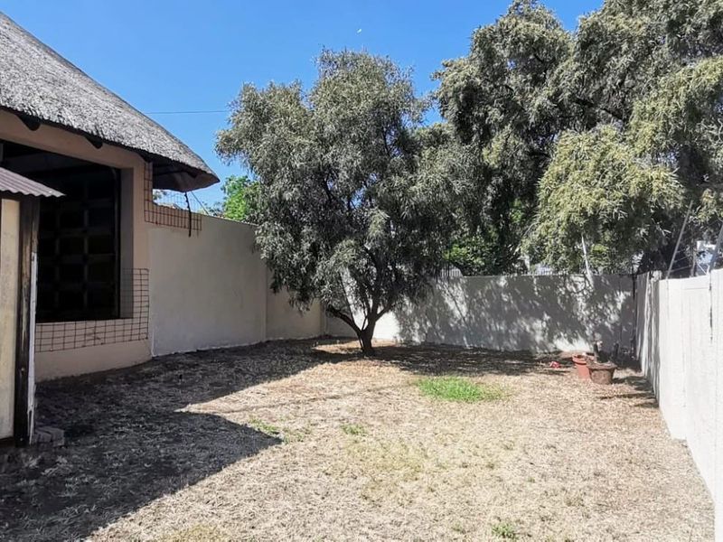 A private rear garden area featuring a thatched roof structure, perimeter walling with electric fencing, and established trees.