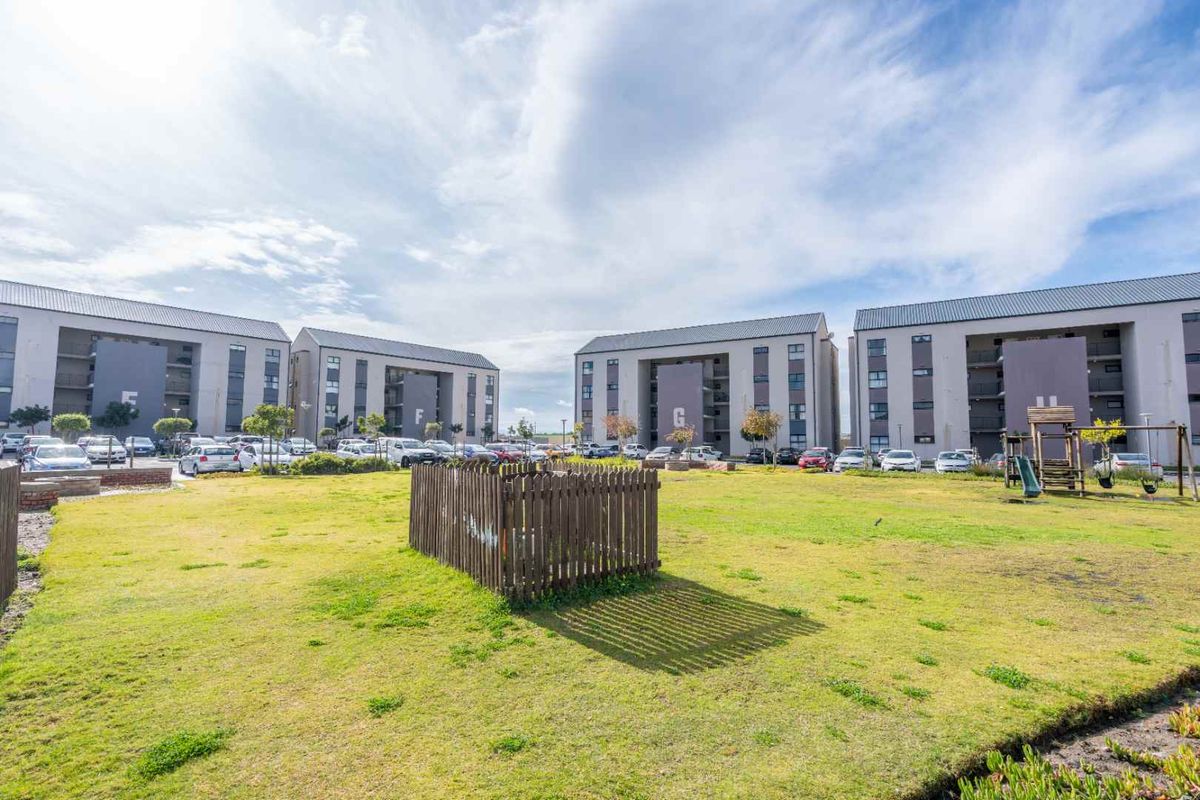 A view of the apartment complex grounds featuring landscaped lawn areas, paved parking, and communal outdoor space between the residential buildings.
