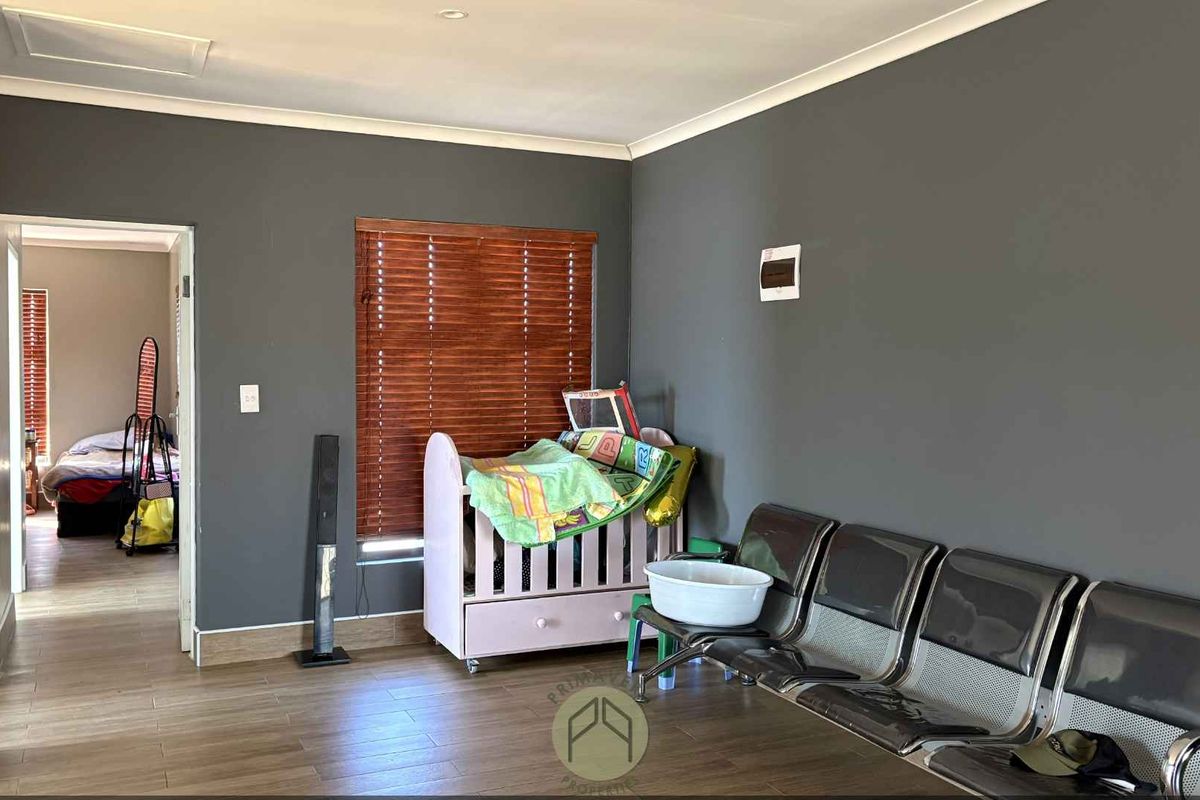 A living room featuring wood-look tile flooring, dark grey walls, and wooden venetian blinds, with an adjacent bedroom visible through the doorway.