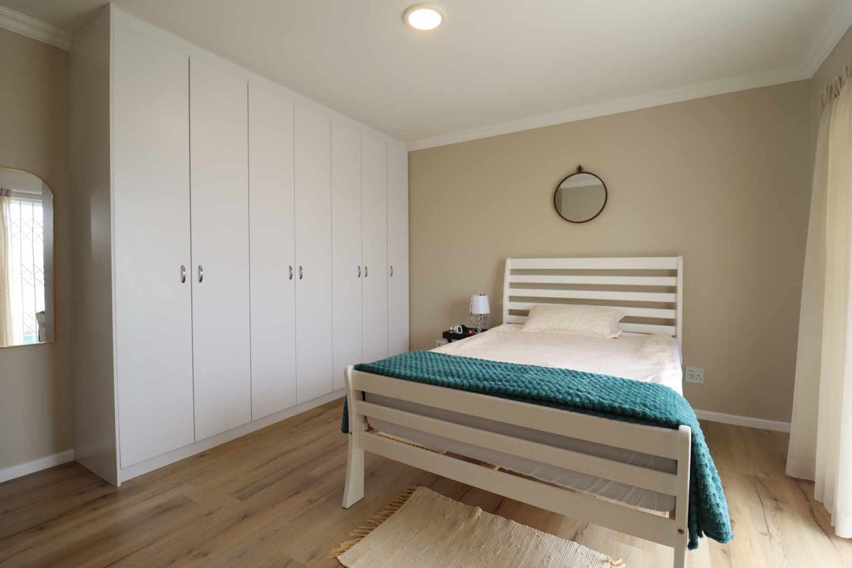 A well-maintained bedroom featuring light wood-look flooring, neutral wall tones, and extensive floor-to-ceiling built-in cabinetry for ample storage.