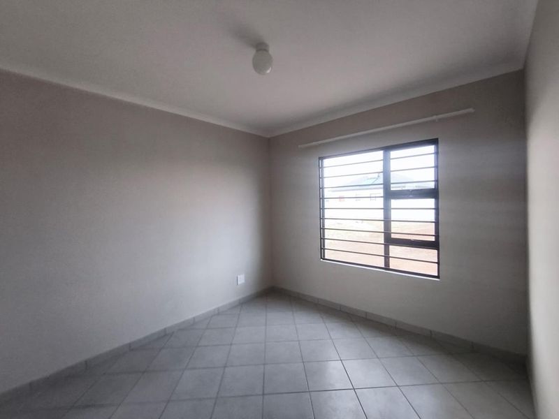 A clean, empty bedroom featuring neutral wall tones, tiled flooring, and a window fitted with security bars.