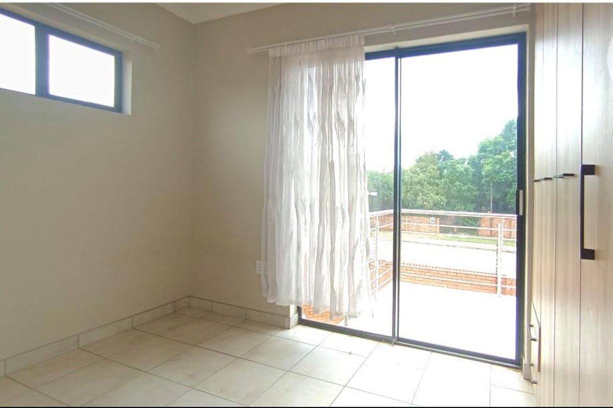 A bright bedroom featuring tiled flooring, built-in wooden cupboards, and a sliding glass door providing direct access to an outdoor balcony area.
