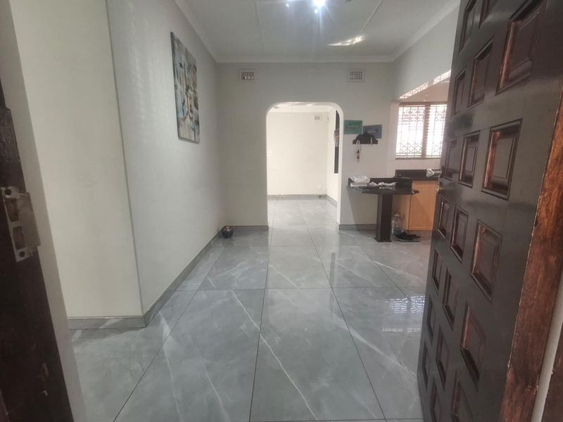 An inviting entrance hall featuring modern grey marble-look floor tiles, an open archway leading to the living area, and a built-in breakfast bar.