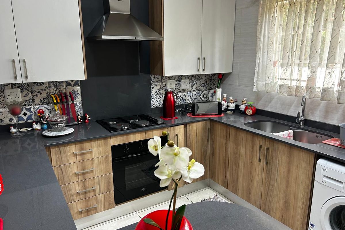 Modern kitchen featuring wood-grain cabinetry, dark stone countertops, built-in oven, gas hob, stainless steel extractor fan, and integrated plumbing for a washing machine.