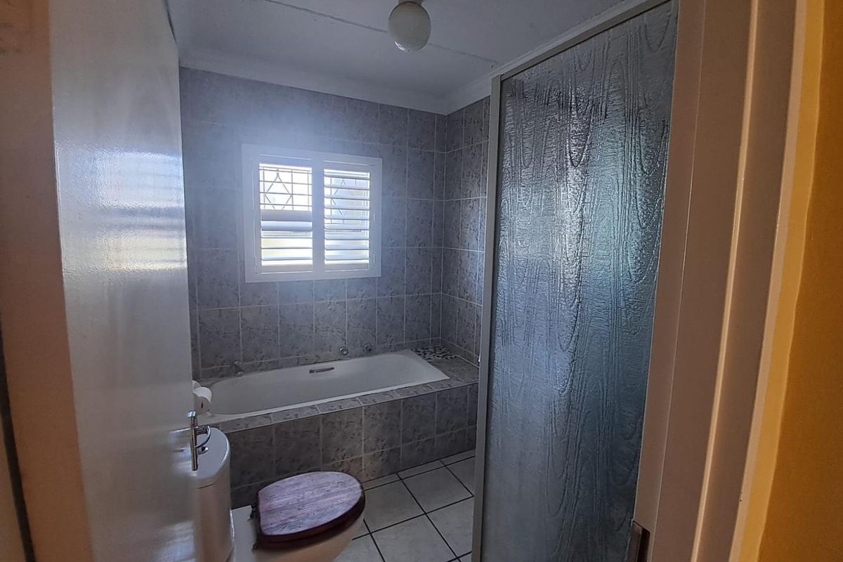 A functional bathroom featuring a built-in bathtub, separate shower enclosure, and tiled finishes throughout, offering a clean canvas for potential modernization.