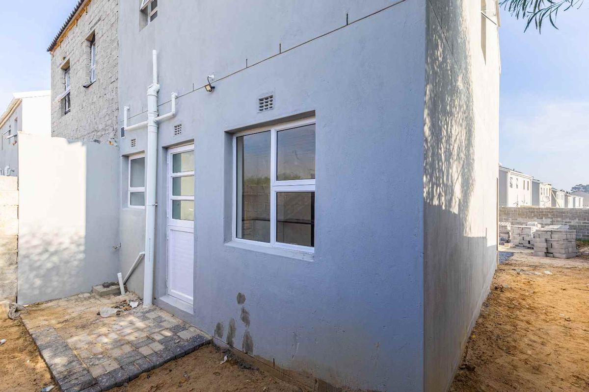 Rear exterior view of the townhouse featuring a paved utility area, white framed windows, and a rear access door.