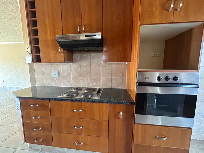 A functional kitchen featuring wooden cabinetry, granite countertops, a built-in oven, electric hob, and an extractor fan with a tiled backsplash.