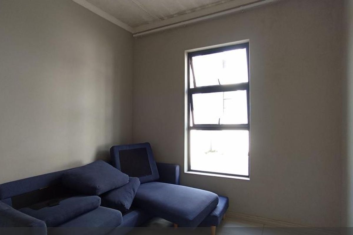 A simple living room featuring neutral walls, tiled flooring, and a large window providing natural light.