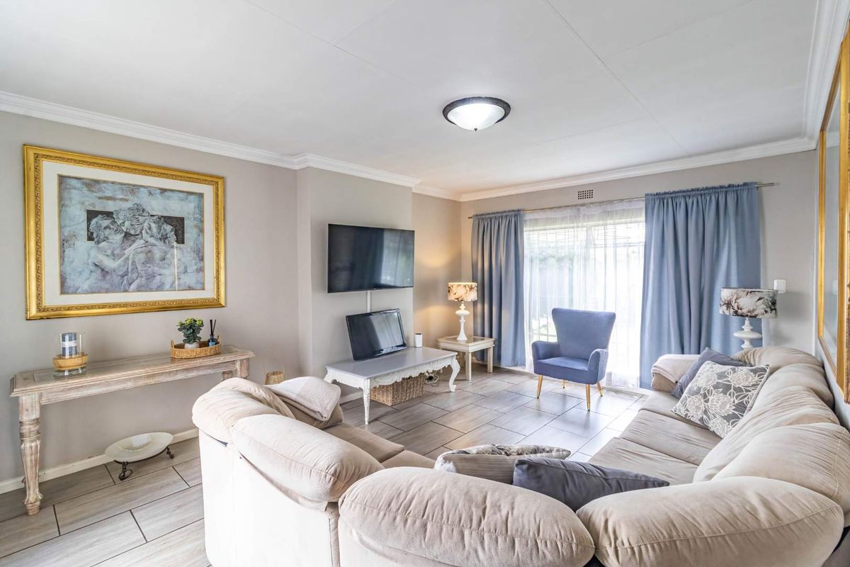 A well-maintained living room featuring neutral tiled flooring, decorative ceiling cornicing, and a large sliding glass door providing natural light.