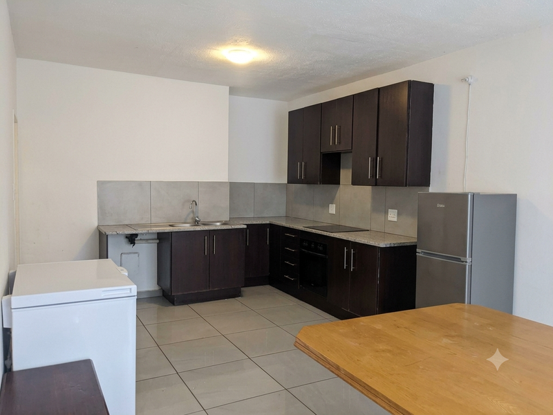 A functional kitchen featuring dark wood cabinetry, granite countertops, a built-in oven, electric hob, and tiled flooring.