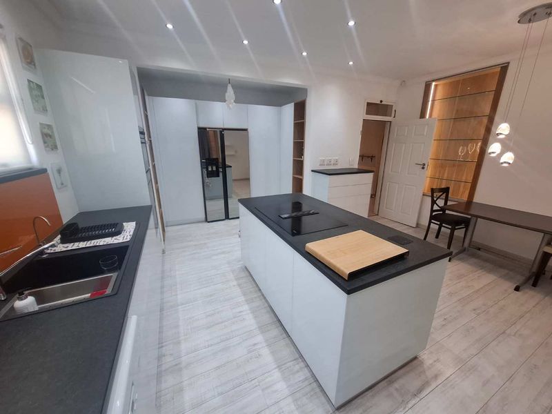 Modern kitchen featuring a central island with an induction hob, sleek white cabinetry, dark countertops, and recessed lighting, creating a clean and functional workspace.