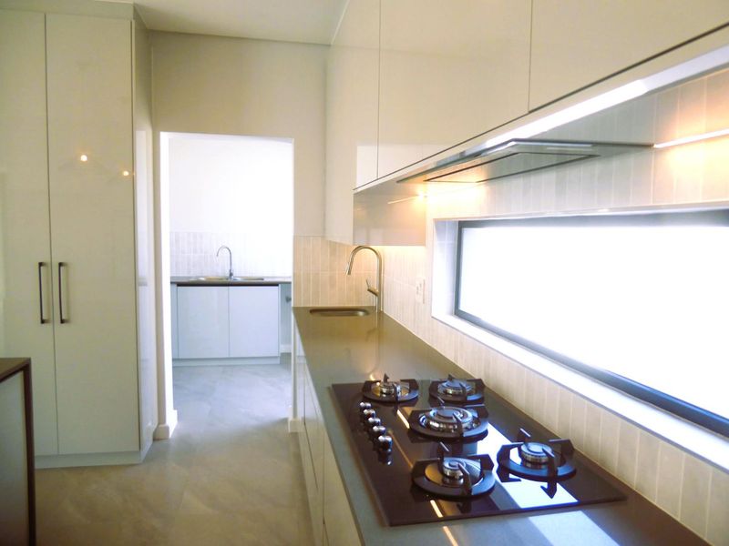Modern kitchen featuring sleek cabinetry, stone countertops, a gas cooktop with integrated extractor, and a separate scullery area visible in the background.