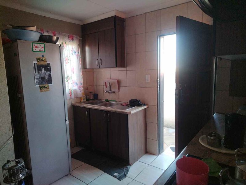 A compact kitchen featuring dark wood-look cabinetry, tiled splashbacks, and a stainless steel sink, with direct access to an exterior area.
