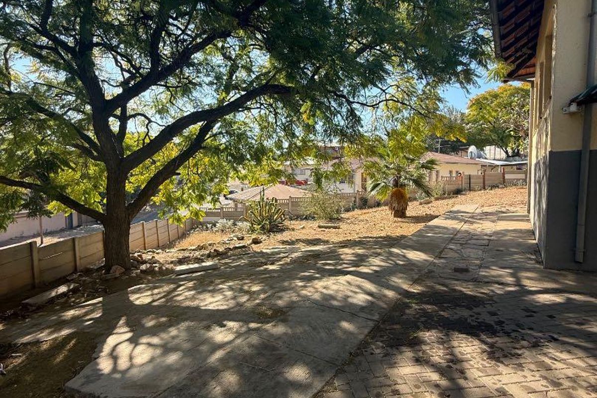 Rear exterior view featuring a paved walkway, concrete patio area, and established trees along the property boundary wall.