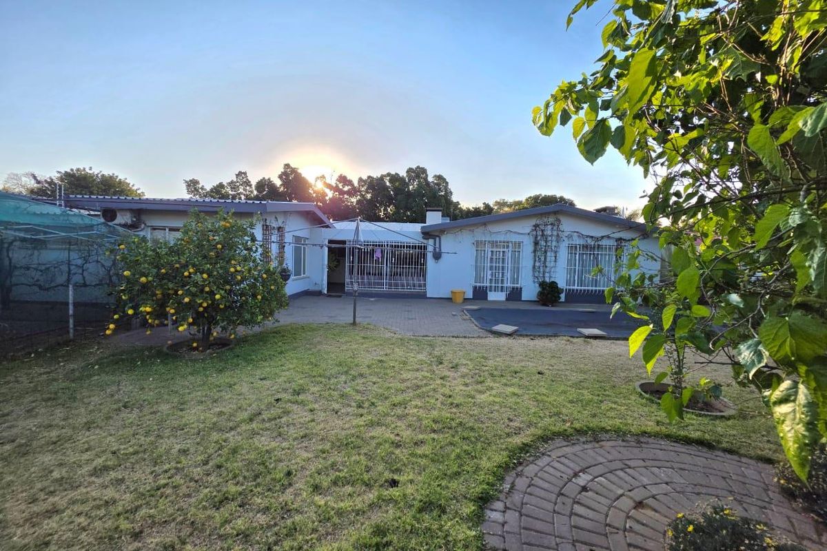 Rear view of the house featuring a paved patio area, security gates, and a well-maintained garden lawn.