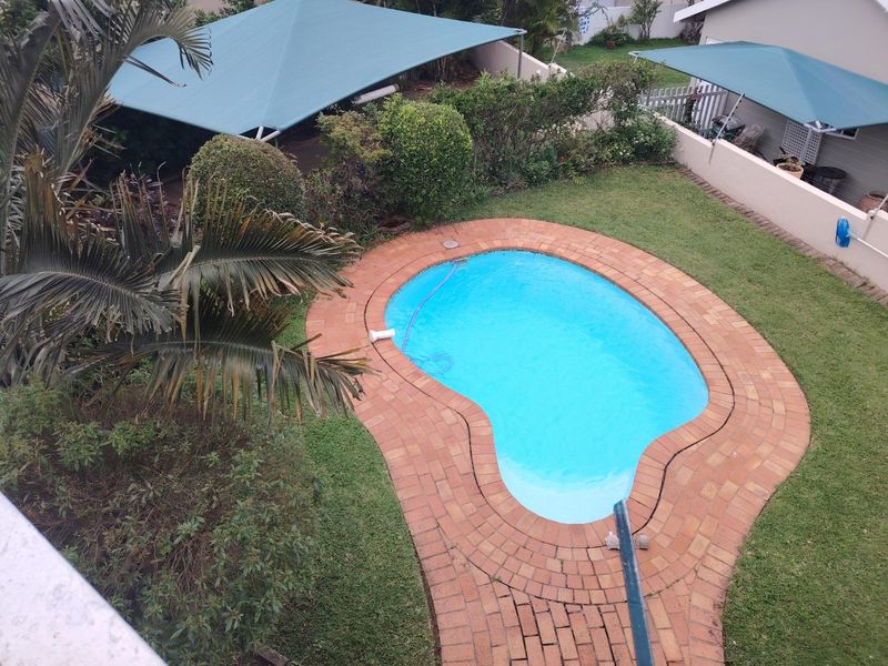 Elevated view of a private backyard featuring a kidney-shaped swimming pool with brick paving, green lawn, and shade sails.