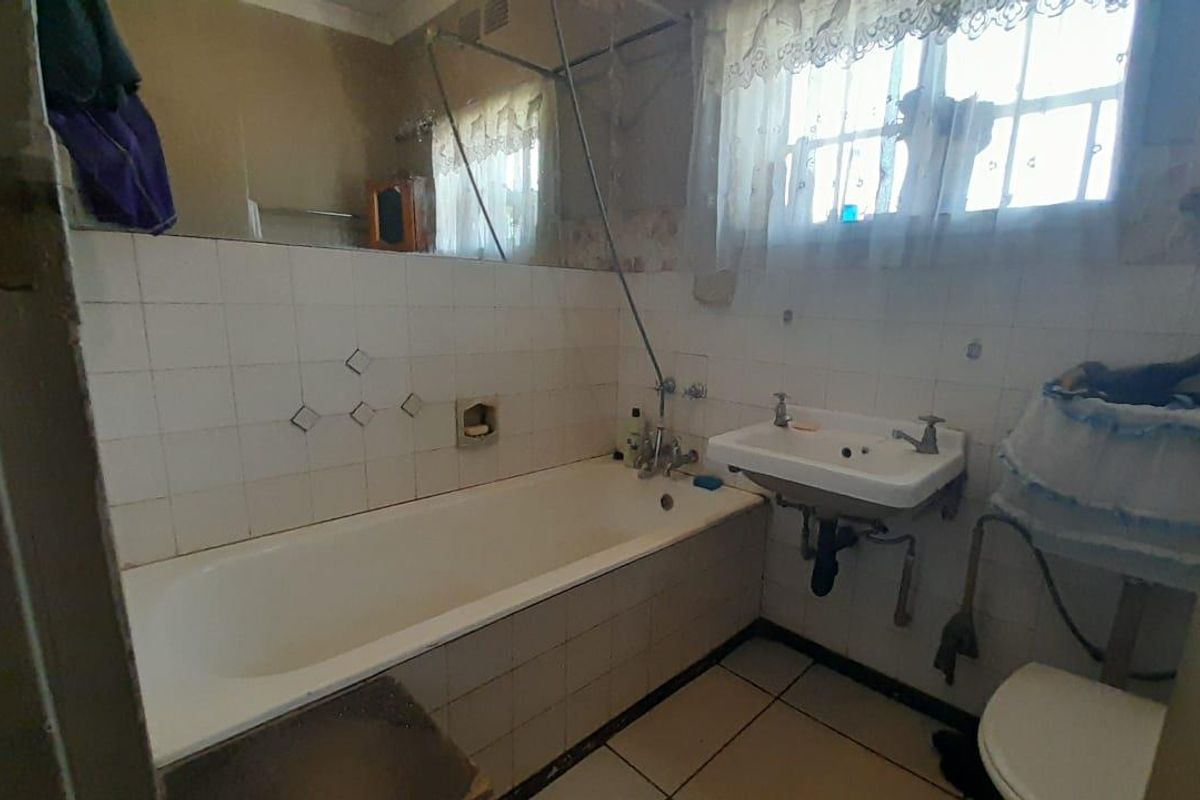 A dated bathroom featuring a built-in bathtub, wall-mounted basin, and toilet, with original tiling and fixtures in need of modernization.