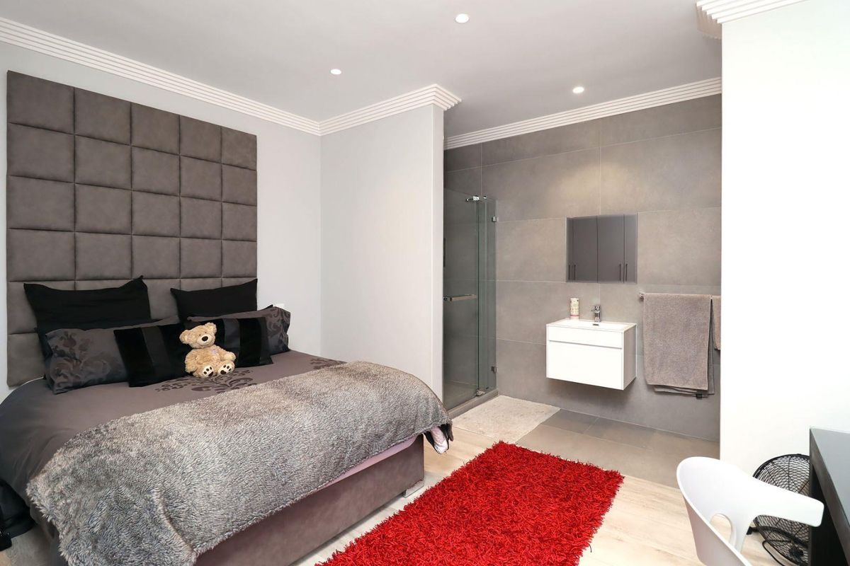 Modern bedroom featuring an integrated en-suite bathroom with a walk-in shower, wall-mounted vanity, and contemporary grey tiling.