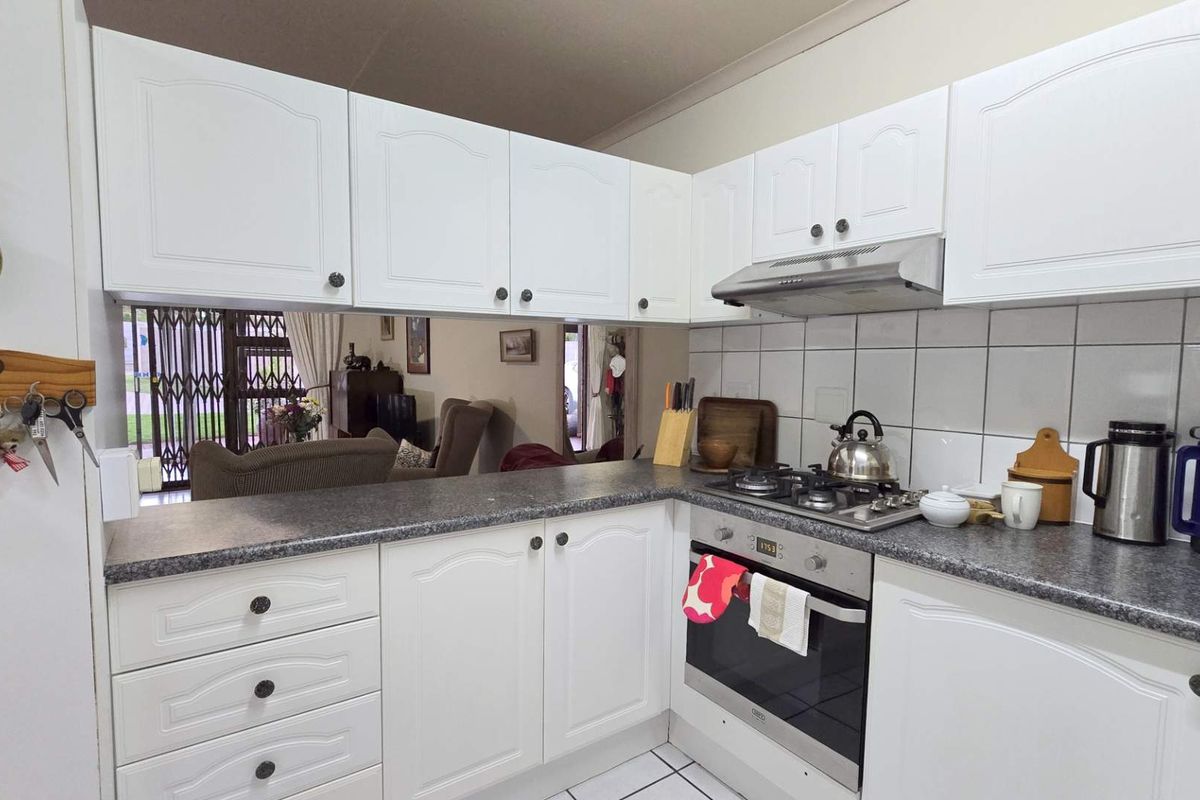 A functional kitchen featuring white cabinetry, a built-in oven, gas hob, extractor fan, and tiled splashback, with a convenient pass-through to the living area.