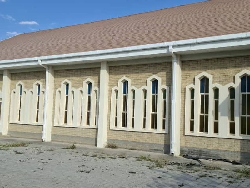 Exterior view of a brick building featuring a pitched roof and multiple gothic-style windows, set above a paved area.