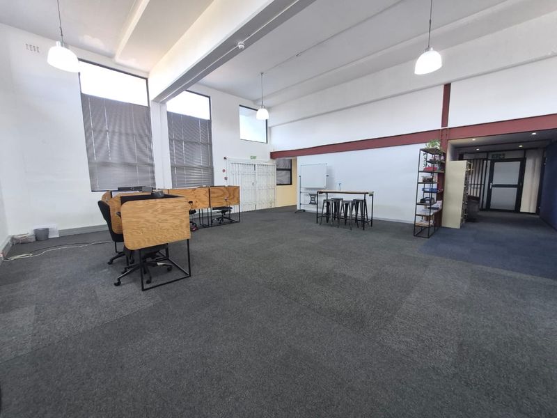 Spacious open-plan office area featuring high ceilings, large windows for natural light, and durable carpeting, suitable for a collaborative workspace.