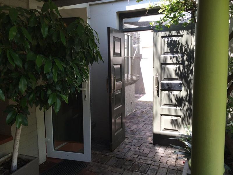 A covered patio area featuring brick paving, panelled timber doors, and a security gate, providing access to the exterior of the cottage.