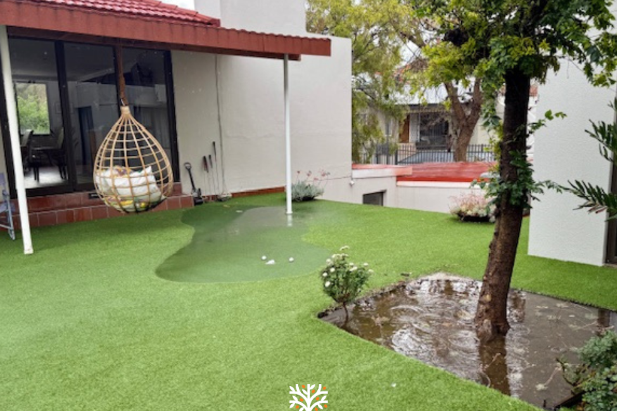 A rear garden area featuring artificial turf, a small putting green, and a covered patio space with direct access to the interior.